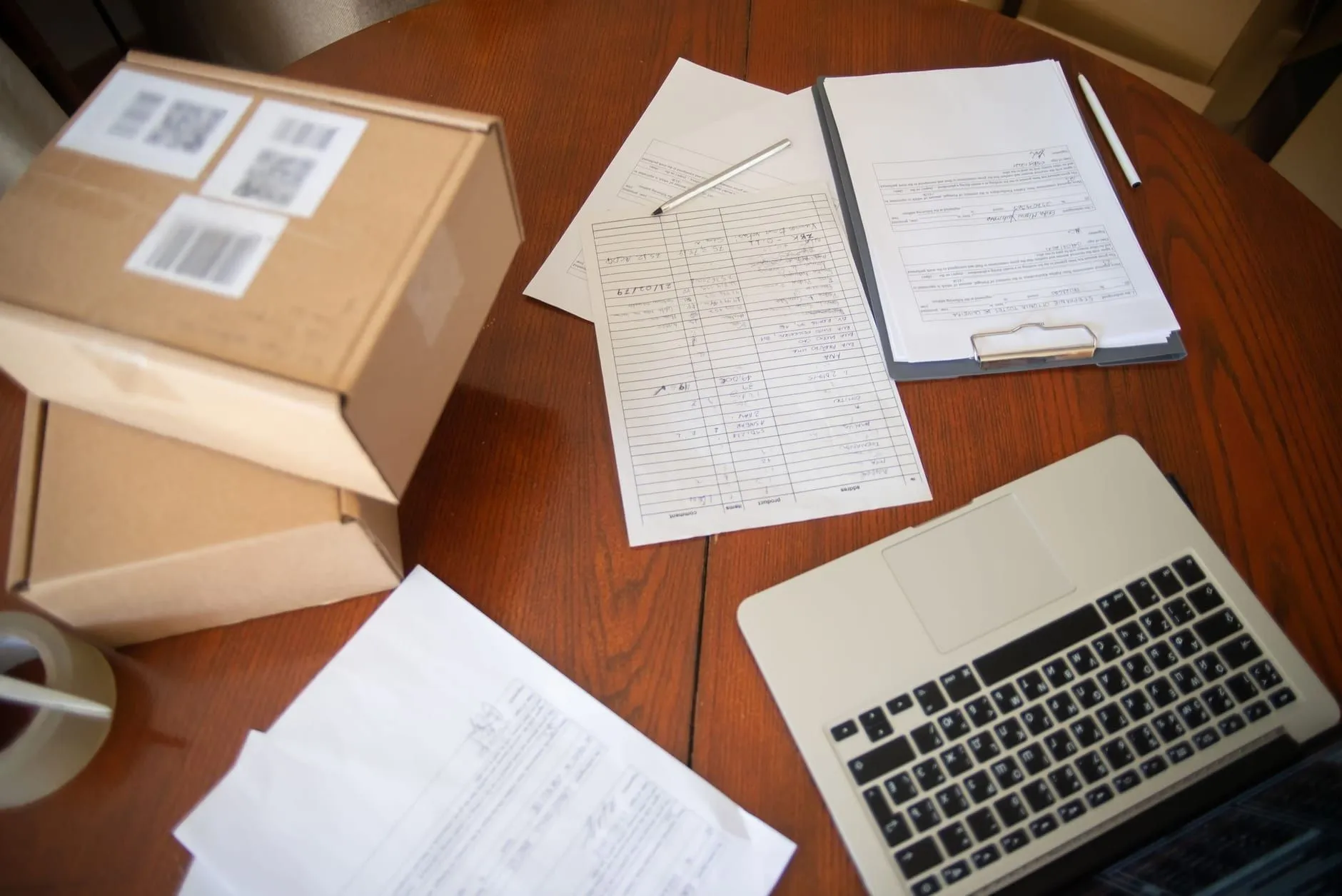 Escritorio con formularios en papel, cajas de envío y una portátil